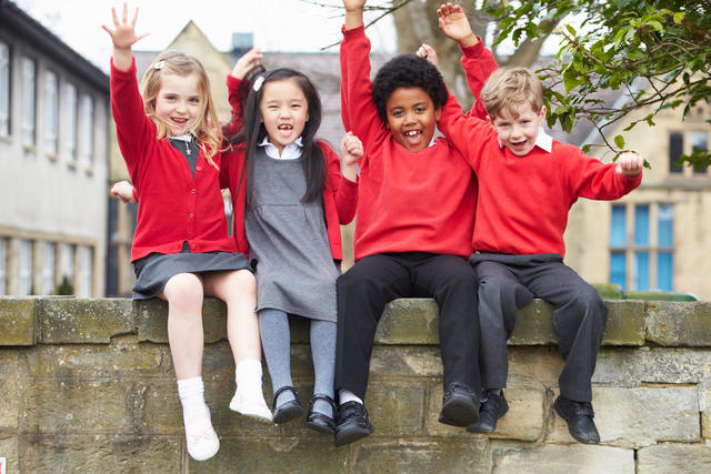 Happy young school children sitting on a wall